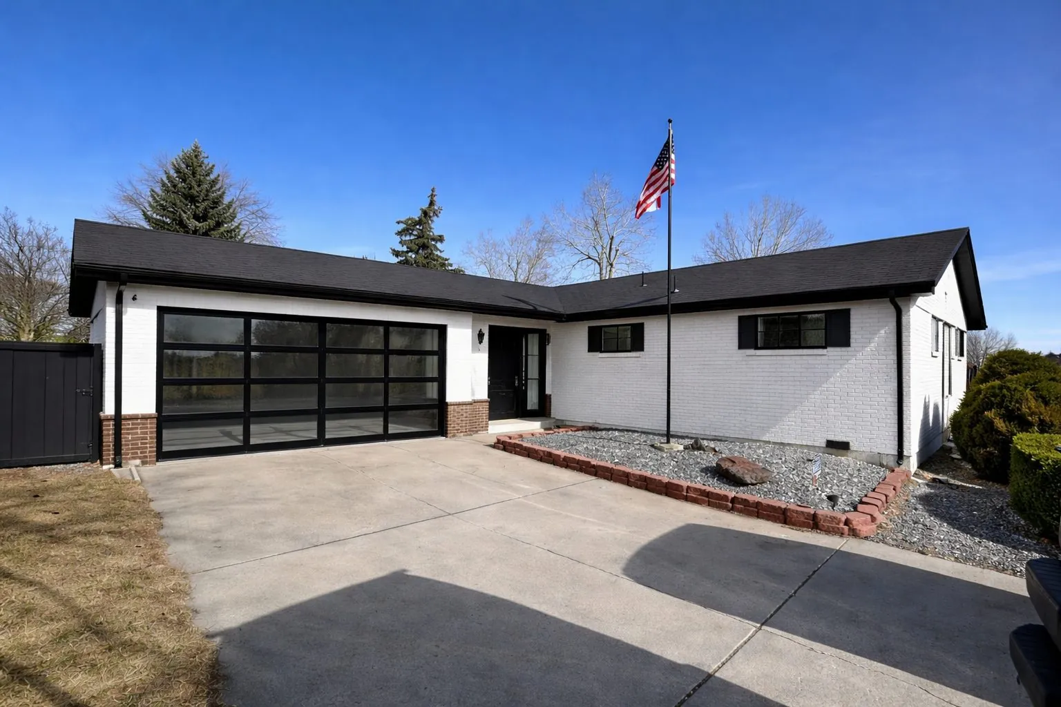 Renovated white brick ranch home with glass garage door and flag