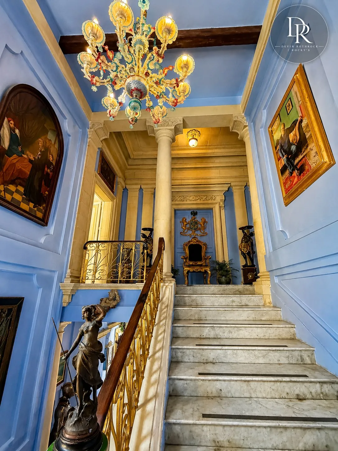 An ornate blue-and-gold grand staircase with chandelier and marble steps