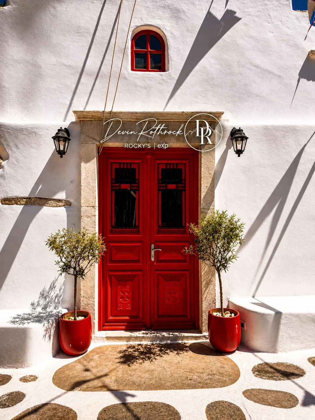 A vivid red Mediterranean doorway framed by whitewashed walls and olive trees